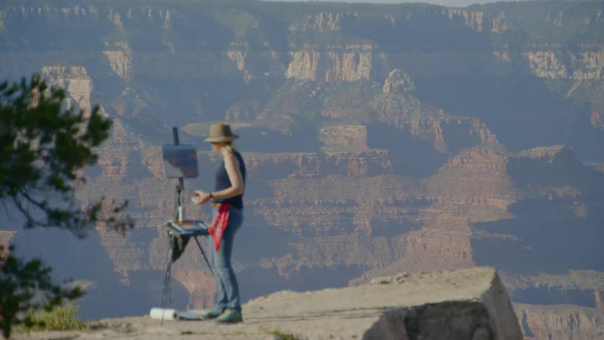 A woman stands on a cliff and paints the landscape in front of her