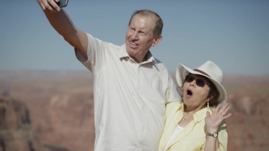 A man takes a photo of himself with his wife near a canyon