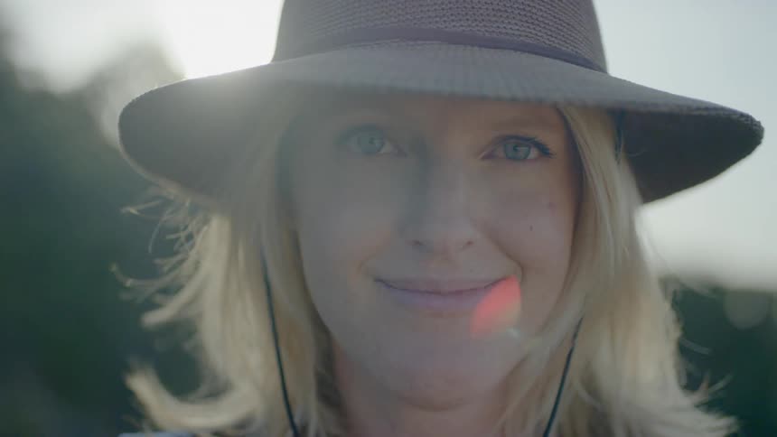 Blonde woman wearing cowboy hat looks around and smiles outdoors