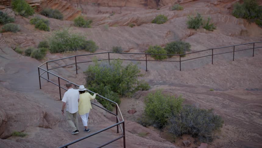 Man and woman walking on a trail guided by some hand railing that the woman is using to help her along
