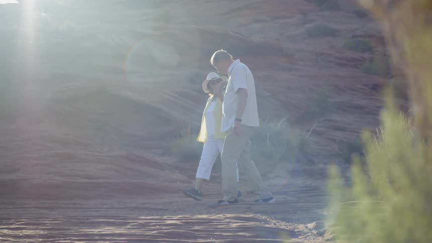 Senior man and woman holding hands walk through canyon on a sunny day