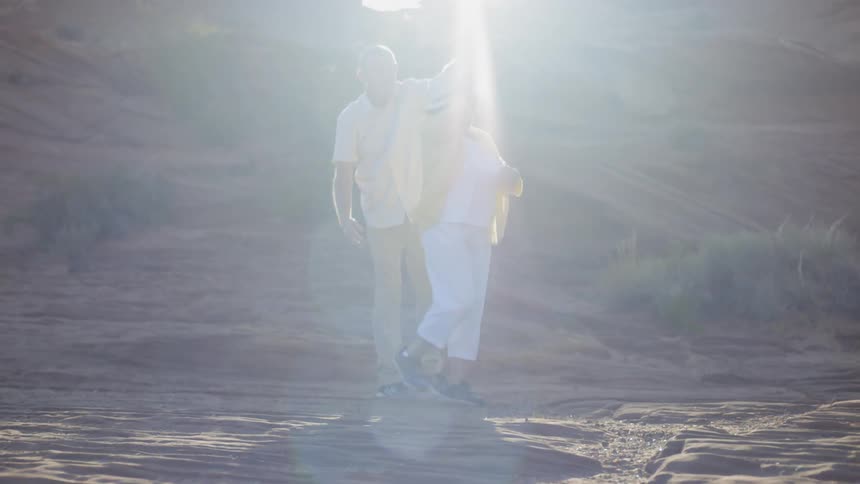 An elderly man and woman dance in the rocky desert