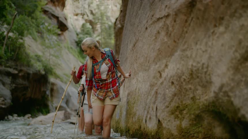 Two women and a man wade through the water as they hike