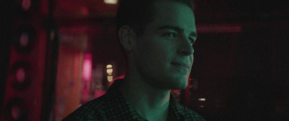A white man stands in a dark room and looks around before smiling