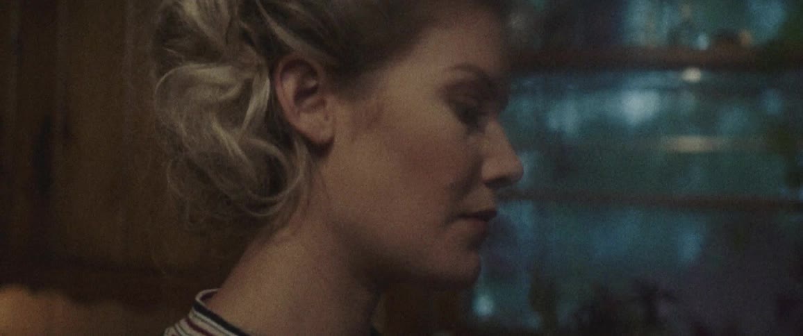 Blonde woman stands and looks down indoors at dusk