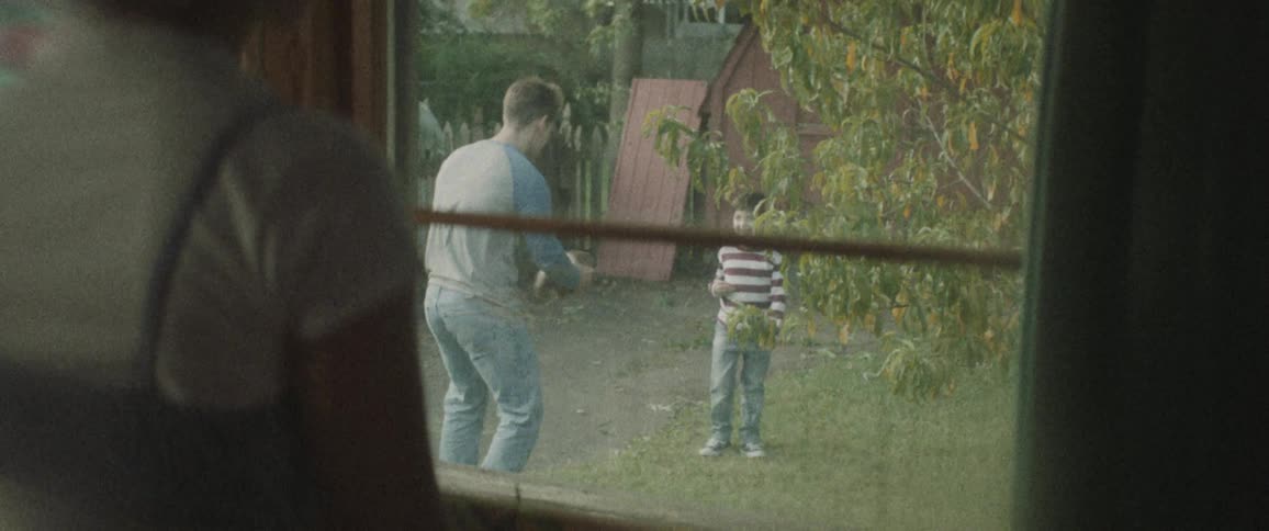 A woman stands at the window and watches as a man and little boy throw a football together