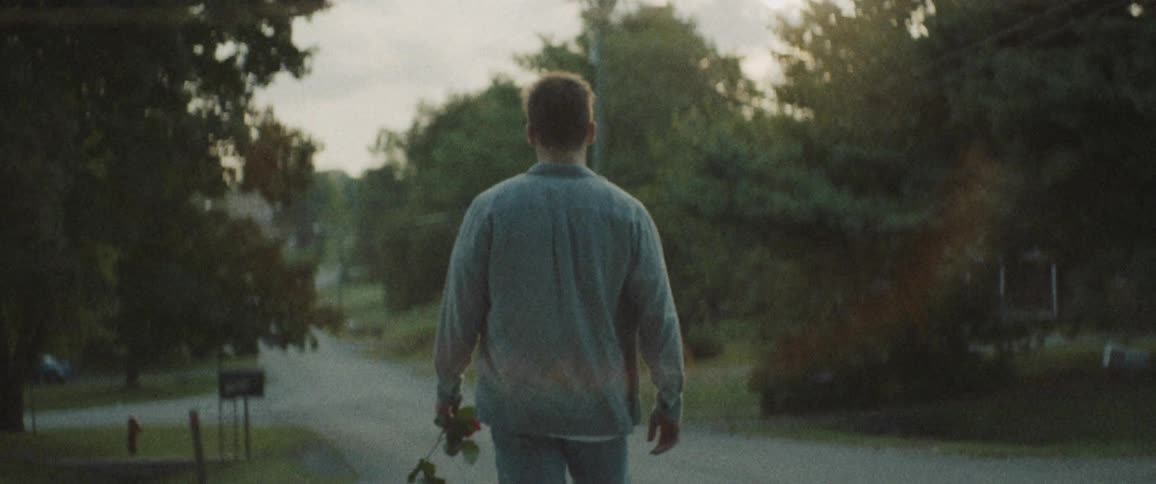 A white man holding a rose while walking down a road