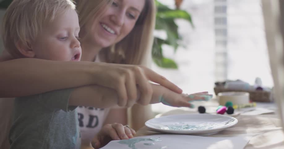 Mom showing son how to make handprints with blue paint