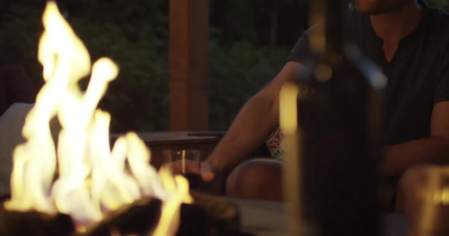 A man drinks from a cup in front of a fire