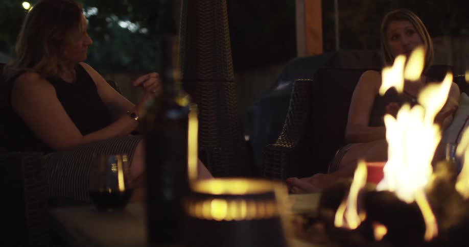 Friends sit next to an outdoor fire and chat