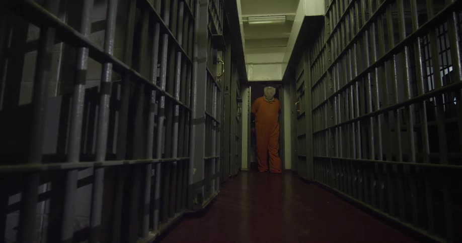 Guard bringing a hooded prisoner into a cell