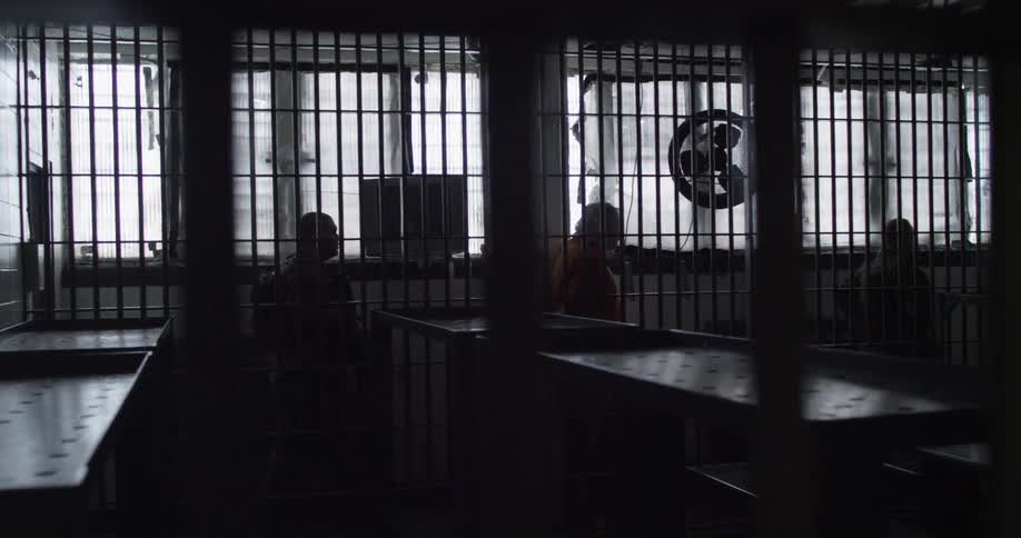 Prisoners are being led down a hall behind some bars
