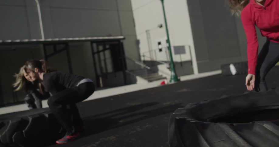 Women in athletic clothes work at flipping massive tires