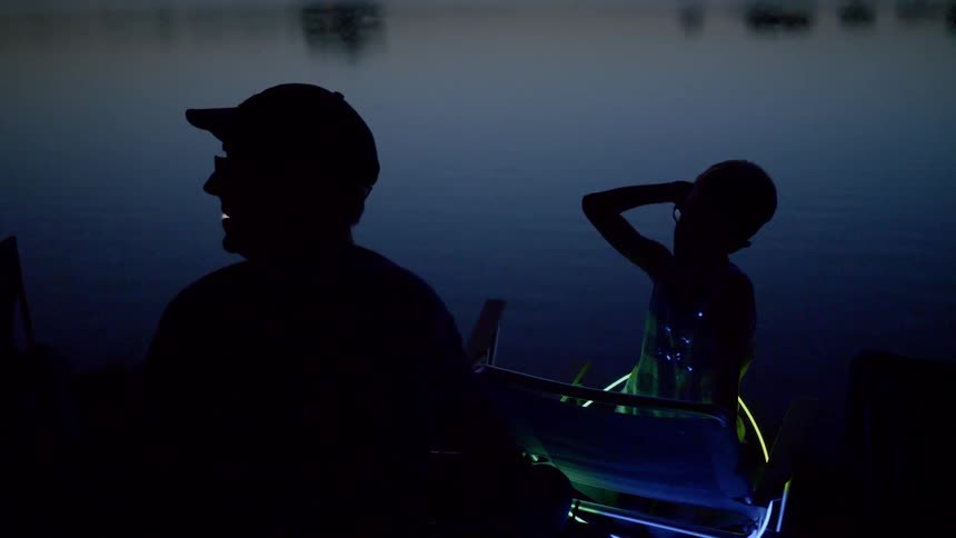 A man and a child sitting at lakeside in the dark at night