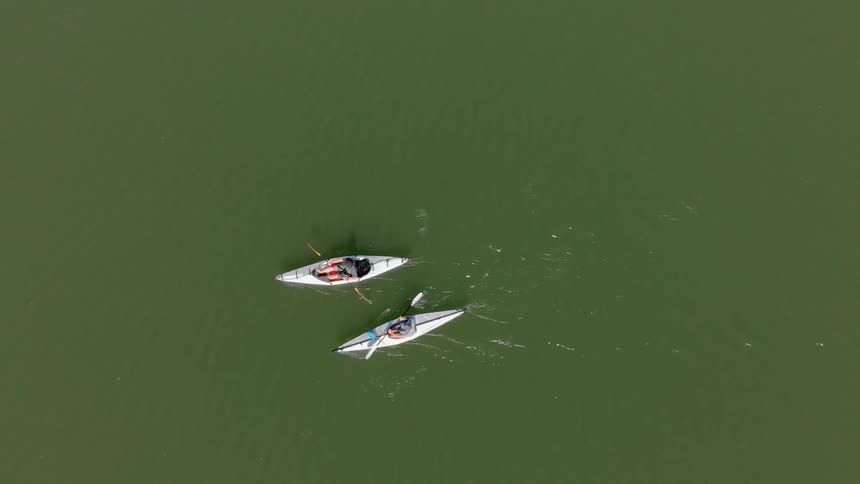 Two people are using paddles to move individual kayaks through a body of water