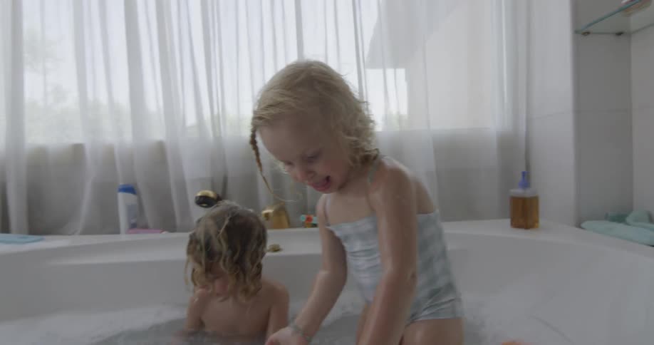 Two young children in their swimsuits are playing and splashing in a large bathtub