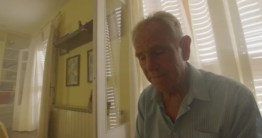 Old man sitting on the chair looks down at the picture in a room
