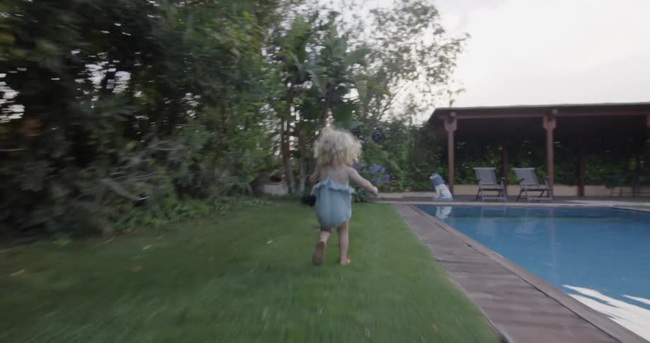 Blonde toddler girl runs to the dog next to the pool