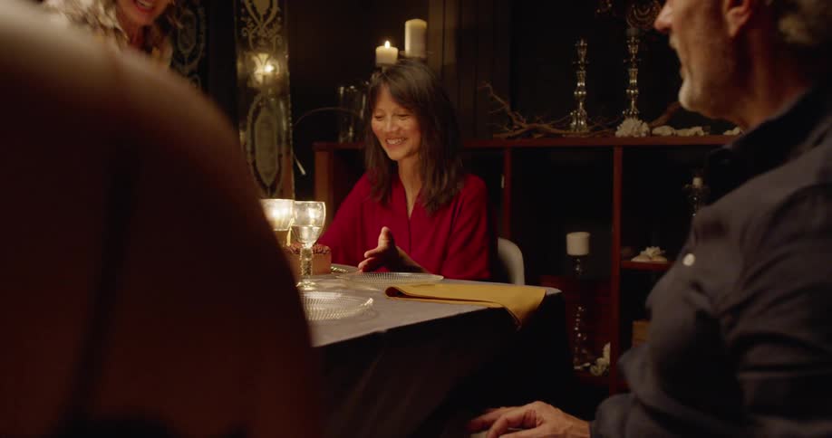 A younger woman sets a cake in front of an older woman at a dinner table and the rest of the family watches