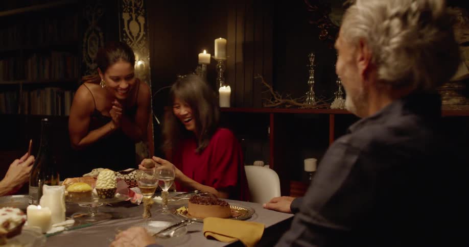A group of people sitting at a dining table laughing as a woman unwraps a wooden object