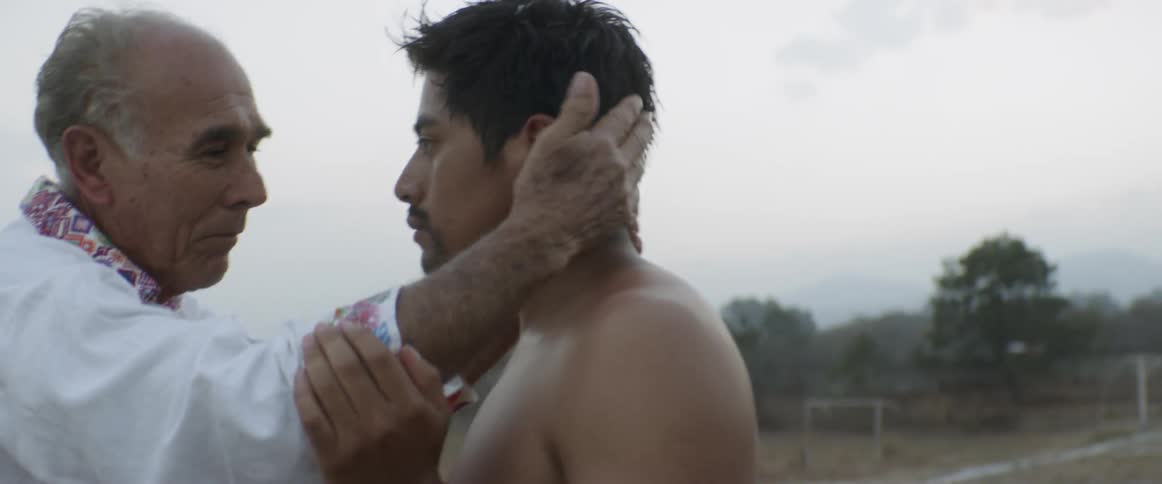 Older man speaks to younger man then they hug outdoors