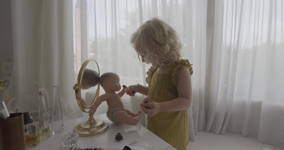 A girl puts lipstick on a doll