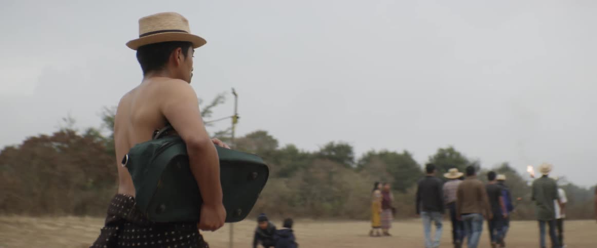 A man without a shirt walks behind a group of men some of which carry torches