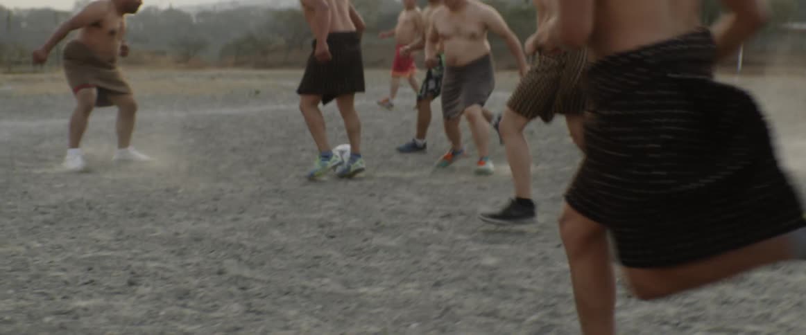Men play soccer in a dirt field