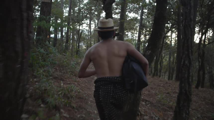 Shirtless muscular man wearing hat runs in the woods
