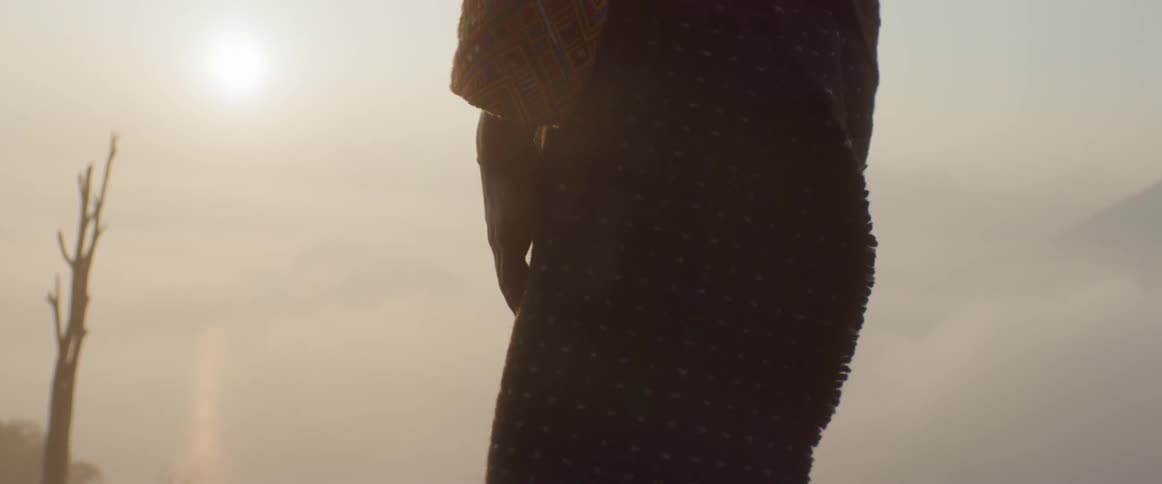 A person wearing traditional clothing stands under a harsh sun
