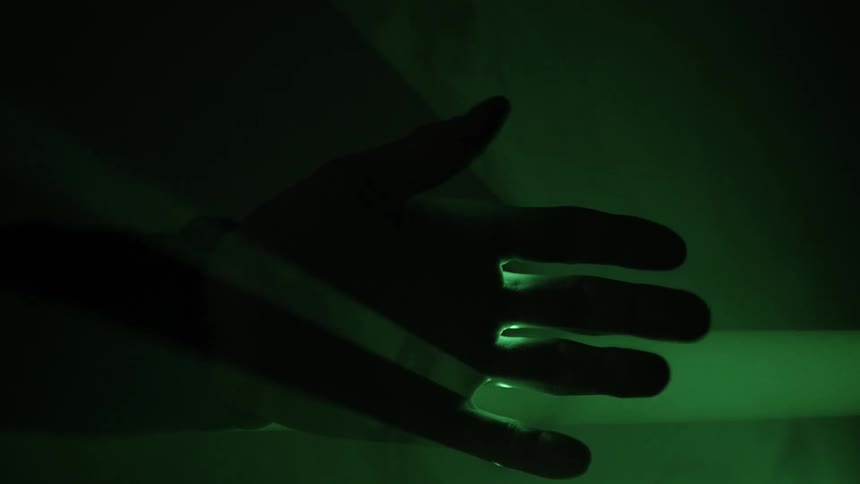 A mans fingers piercing a green laser sheet of light