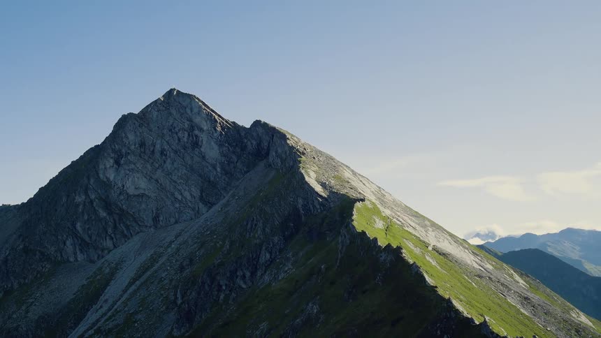 Grass grows to the very top of a sharp peaked mountain in a large range