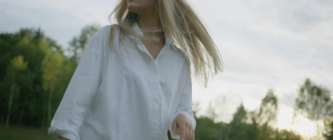 Blonde woman wearing a white shirt runs on the grass in the field at sunset