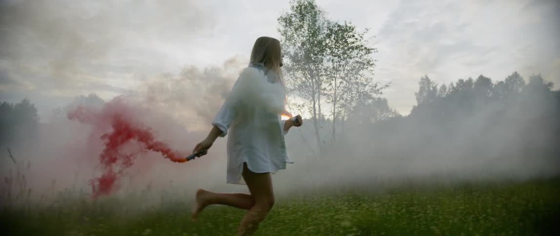 Woman runs in a field as she disperses colored smoke