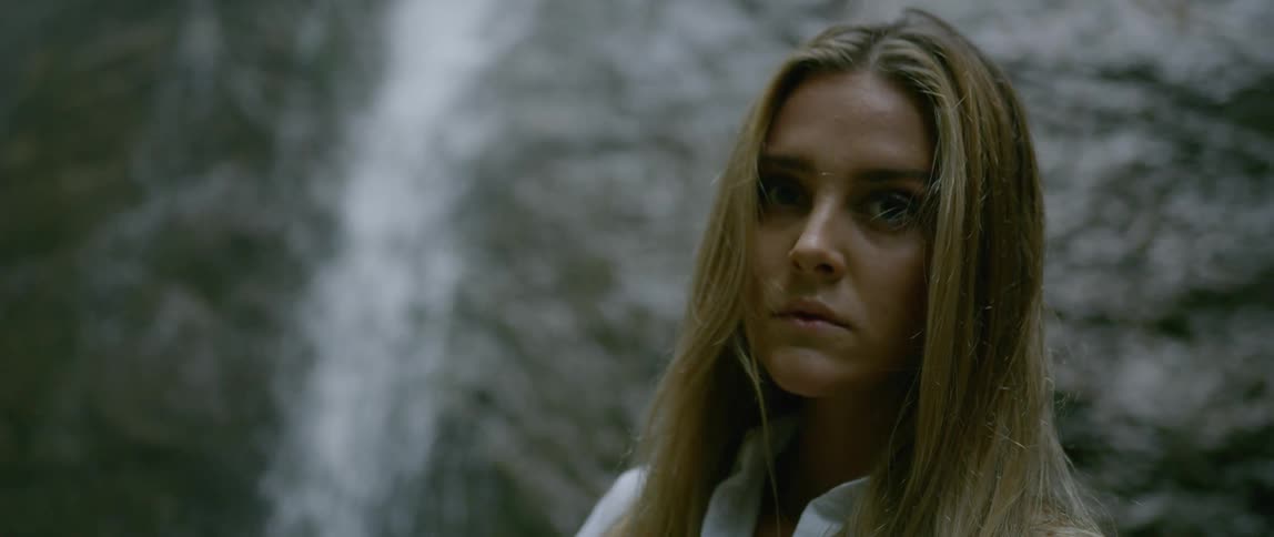 Blonde woman looks up at the water fall and turns to the camera