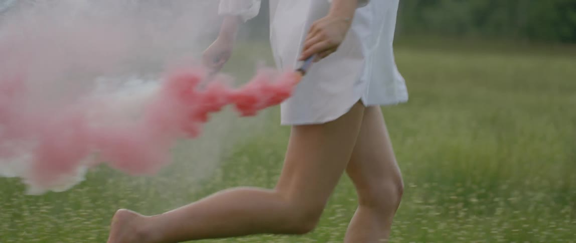 A woman runs holding two fire crackers blowing pink smoke