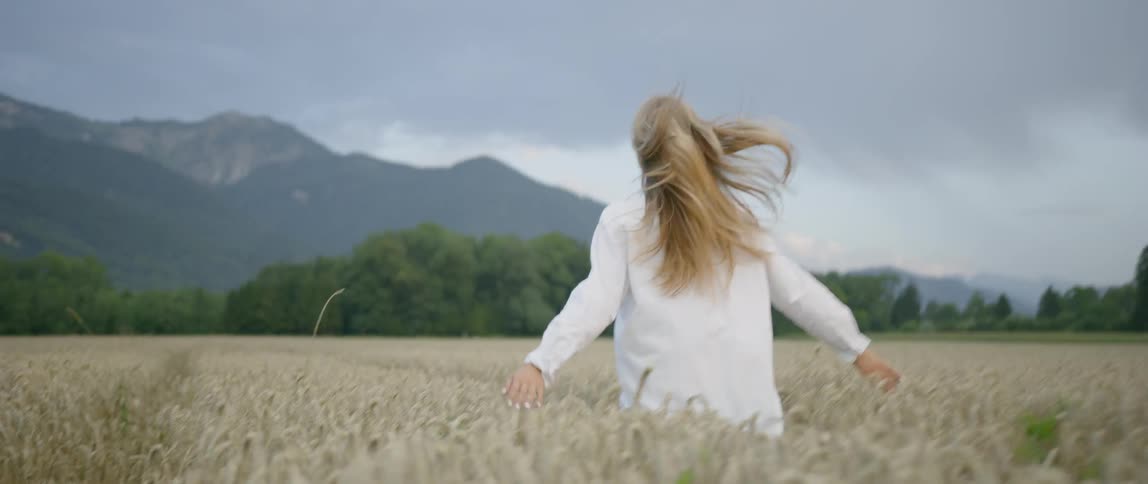 Blonde woman wearing a white suit runs along the field of wheat