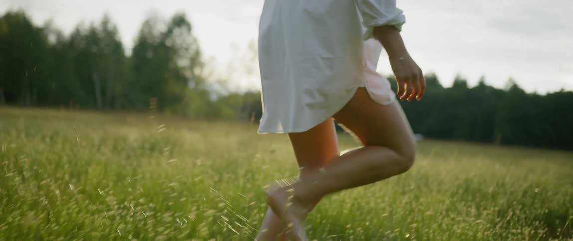 Woman wearing a white shirt runs along the grass in the field at sunset