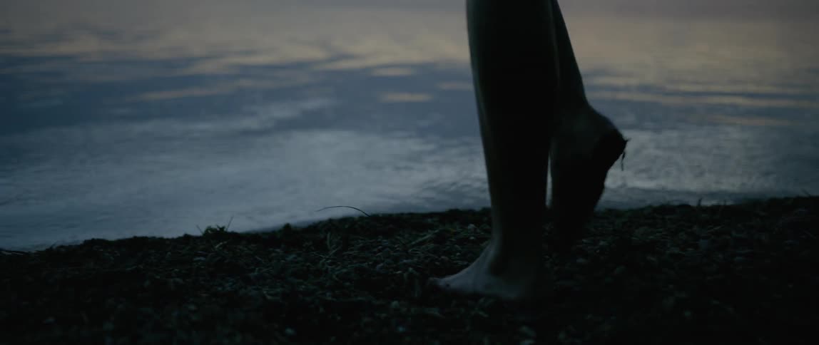 Woman walks barefoot through muddy bank and into water