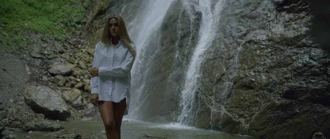 Woman wearing a white shirt stands in front of the waterfall in the forest