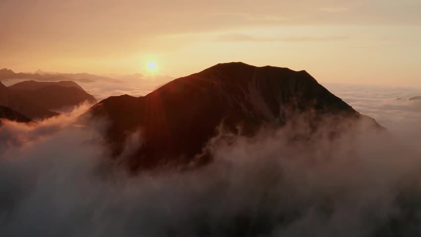 The sun sets as clouds float along side mountains