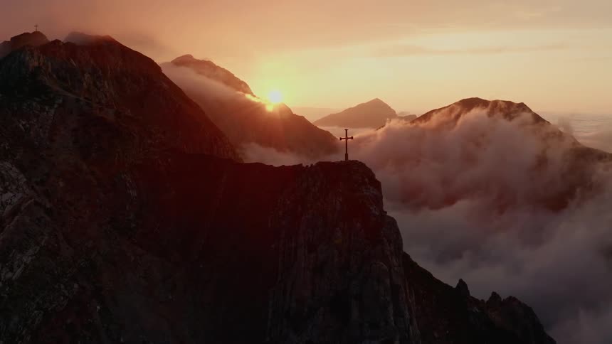 A large cross atop a snow and cloud covered mountain peak