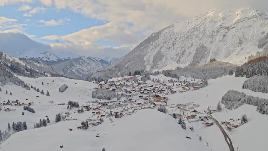 Snow covers town and surrounding mountains under cloudy sky
