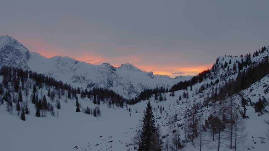 The sun sets behind a snow covered mountain range