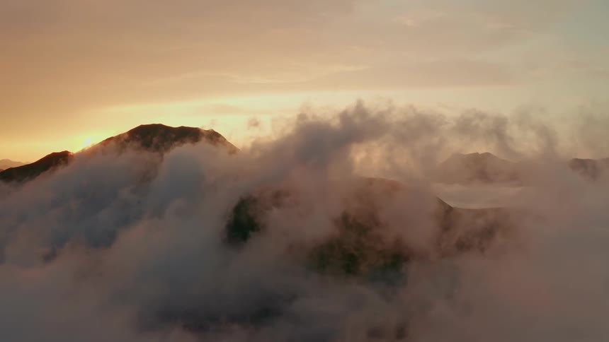 White fluffy clouds in the sky envelope all but the very peak of a tall mountain