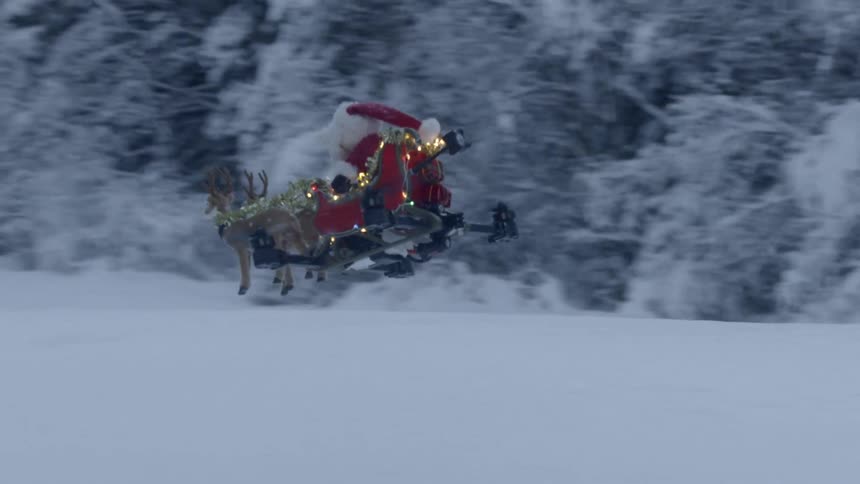 A drone with santa claus and reindeer decoration on top flying through a snowy landscape