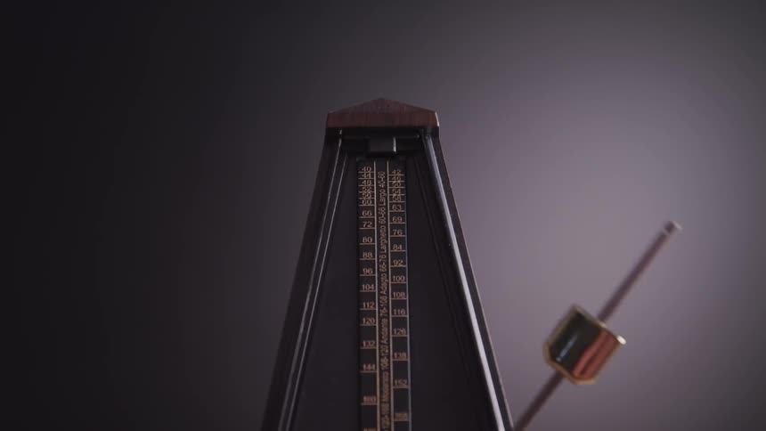 The metallic arm of a mechanical metronome swings back and forth