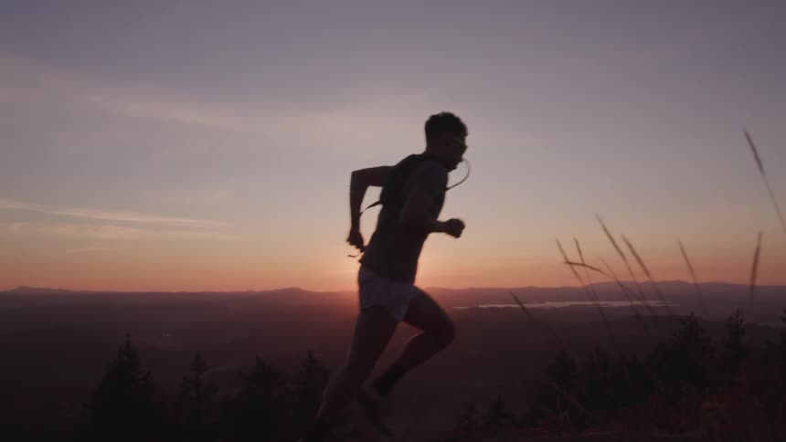 A male jogger running outside with the sun in the background
