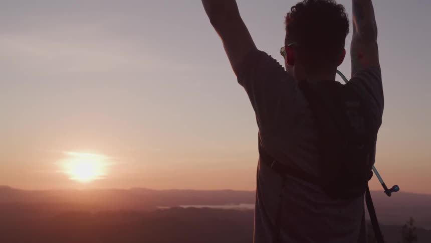 Man raises hands in a victorious gesture at sunset