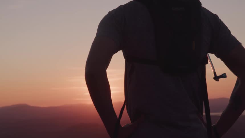 A scenery of a man standing towards the sun at the mountain peak